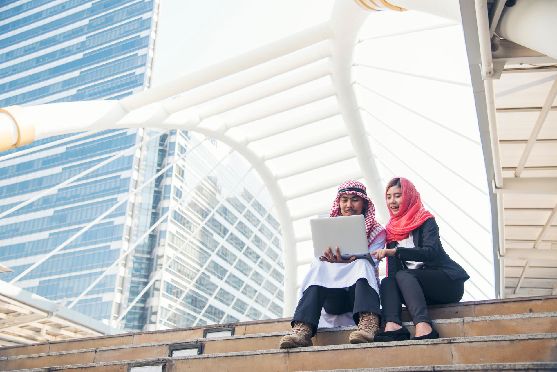 Arab team hold laptop computer uae union teamwork people. Smart arab group of people using computer laptop look at screen happinessmodern muslim UAE city. Entrepreneur Asian people smile team meeting